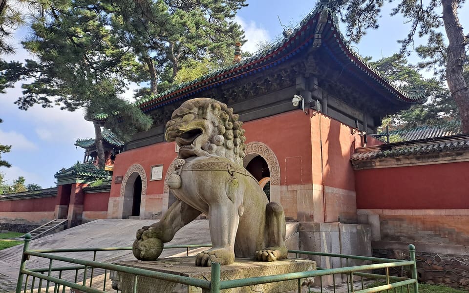 A carved stone guardian lion stands before the red entrance hall of Pule Temple in Chengde