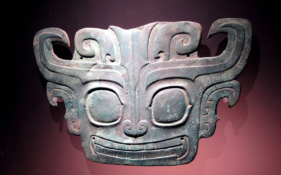 A bronze animal mask excavated from Sanxingdui displayed against a dark museum background