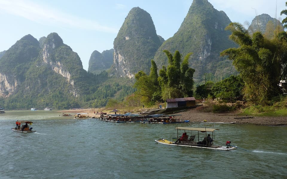 Boats crossing the Li River beneath steep green karst peaks between Guilin and Yangshuo