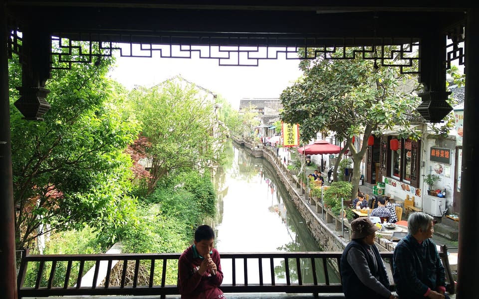 A narrow canal and waterside businesses seen through a covered bridge on Pingjiang Road in Suzhou