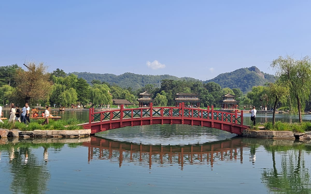 Red footbridge reflected in the lake at Chengde Mountain Resort, backed by pavilions and wooded hills