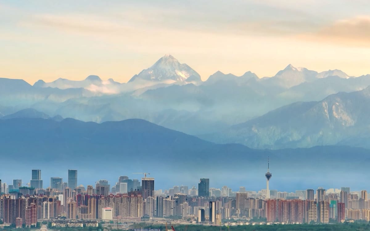 Chengdu's dense skyline beneath layered blue ridges and the snow-capped Mount Siguniang horizon
