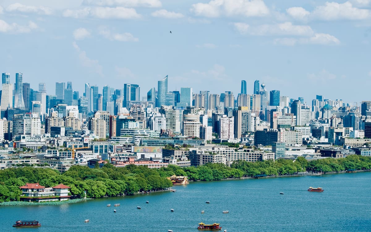 West Lake dotted with sightseeing boats, with green shoreline and Hangzhou's modern skyline beyond