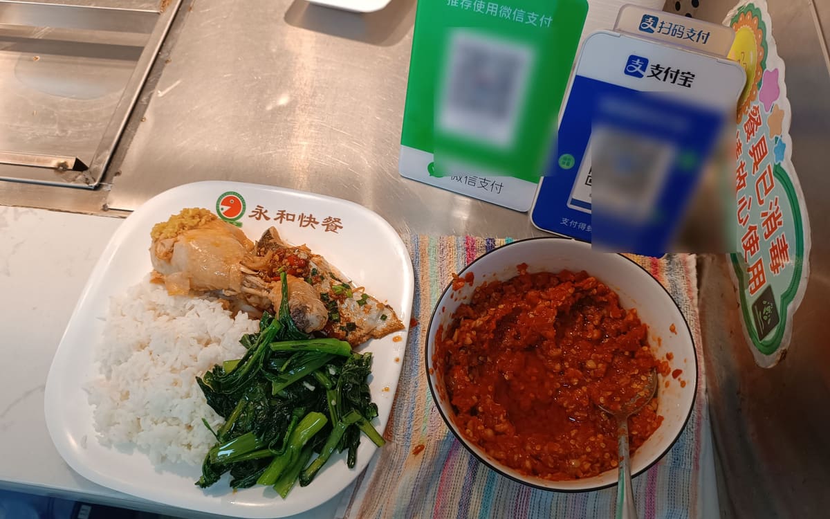 A meal counter in Shenzhen with WeChat Pay and Alipay signs beside a plate of rice and chicken
