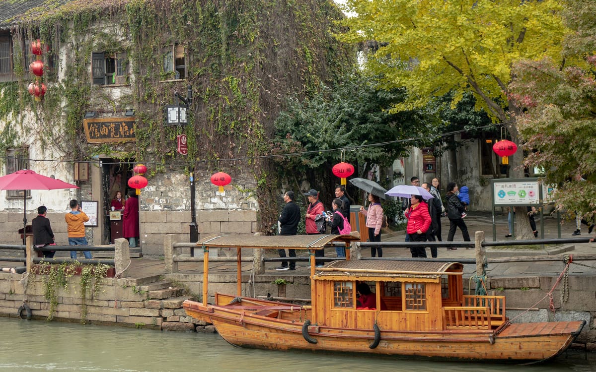Traditional wooden tour boat passing stone houses and autumn trees beside Suzhou's Grand Canal